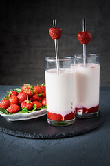 Strawberry milk smoothie in glass with straw on a dark background