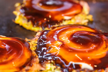 Close-up on an okonomiyaki Japanese omelet, which means cooked to your liking, prepared with shredded cabbage, cooked on both sides on a hot plate and brushed over with oyster and worcestershire sauce