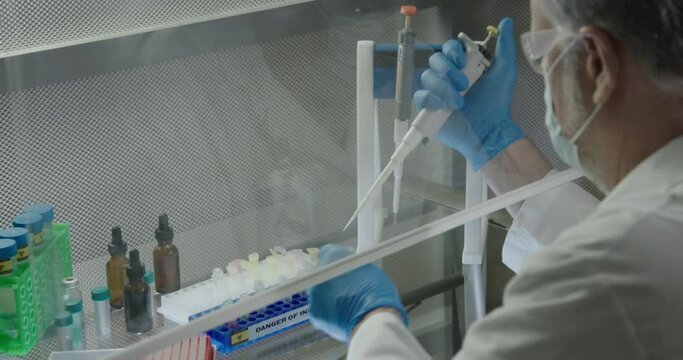 Focus on small snap lock plastic vials under a laboratory ventilation hood while medical technician with a pipette works on preparing pathogen samples.