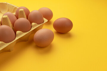 Brown chicken eggs in cardboard box on yellow background