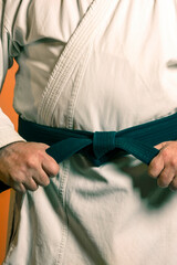 A man is tying a black belt on a white kimon on a background of ora.