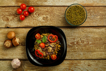On a wooden table is a black dish of boiled mung bean with mushrooms and vegetables.