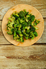 Scattered frozen broccoli on a round wooden board.
