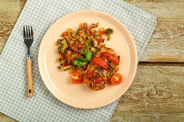 Baked chicken breast with tomatoes and vegetables garnished on a plate with fork on a linen napkin.