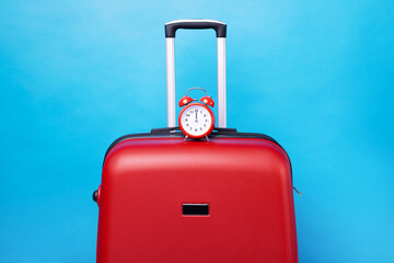 Travel case with alarm clock  over blue background. Time to voyage. Voyage concept. Retro alarm clock with red suitcase