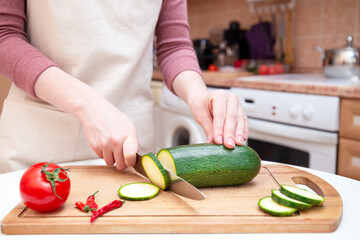 Female hands cut with knife young seasonal zucchini into slices on wooden cutting board. Preparation of vegetables. Seasonal products, harvest. Healthy nutrition, diet. Sliced zucchini