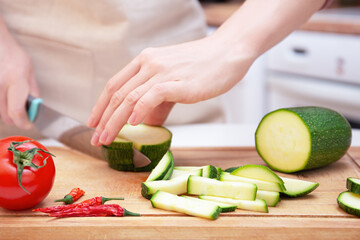 Female hands cut with a knife a young seasonal zucchini into strips on a wooden cutting board. The method of preparation of vegetables. Seasonal products, harvest. Healthy nutrition, diet. 