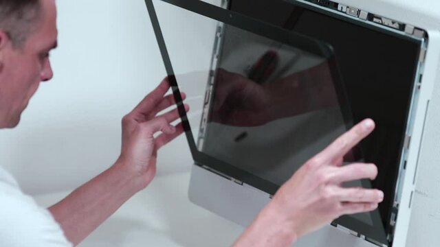 The master puts the monitor glass in place after cleaning. Computer maintenance and repair. Extraction of large particles of dirt from the computer case.