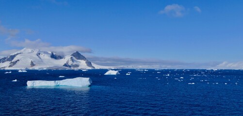Iceberg in blue Antarctic sea, before mountain with blue sky and sun, Antarctica