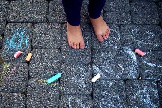 The child paints chalk on the path. Child draws patterns on asphalt. Square chalk of different sizes for drawing. Puffy legs of the baby and multicolored chalk