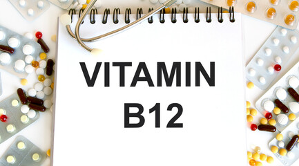 There is an inscription Vitamin B12 on a white notepad, around are multi-colored pills.