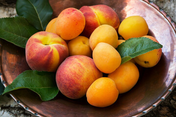 Ripe peaches and apricots on a copper plate and the textural natural wooden background