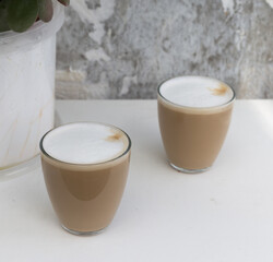 Two Glasses of coffee with cream near the leaves on white background