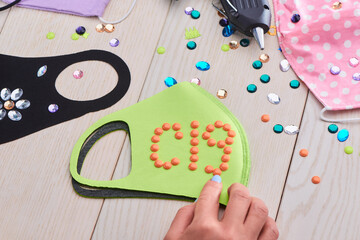 Girl putting a C19 lettering with orange beads on a green face mask