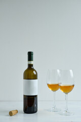 Bottle and two glasses of white wine standing on the white table
