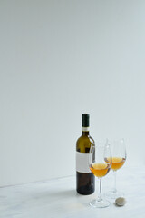 Bottle and two glasses of white wine standing on the white table