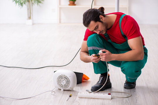 Young Male Contractor Repairing Fan Heater Indoors