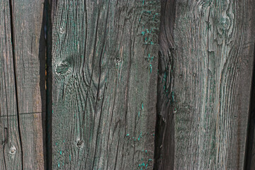 Texture, background: old gray wood with traces of green paint in bright sunlight. Old wooden house.