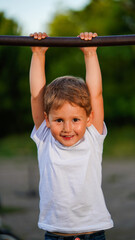 Fototapeta premium Portrait of cute little boy hanging on horizontal bar in summer park