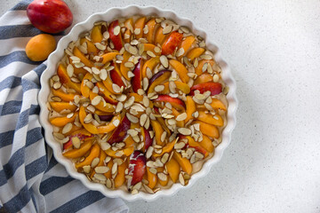 apricot homemade pie, slices of ripe apricots and nectarines on the surface of the dough in a white baking dish
