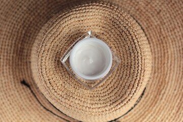 Fototapeta na wymiar Concept of summer skincare. Closeup of a glass jar with cream and a straw hat in the background.