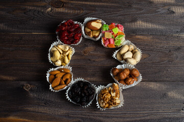 A serving of assorted candied fruit, dried cherries, almonds, raisins, walnuts and hazelnuts in paper muffin cups on a dark wood background. In the shape of a ring.