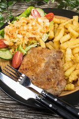 Fried pork chop in breadcrumbs, served with fries and salad.