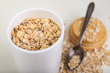 Scattered oat flakes in a ceramic container with a metal spoon. Healthy food prepared for breakfast.