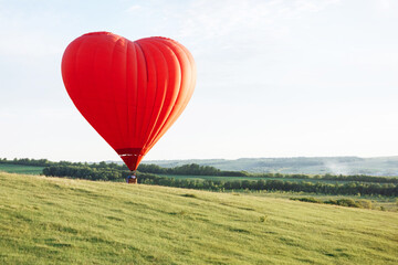 Hot air balloon in the shape of a heart is landing on the green valley