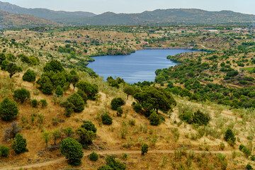 Fototapeta na wymiar blue lake in dry landscape with hills, trees and mountains in the background