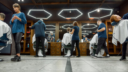 People at barbershop. Team of professional barbers working with clients in the modern loft style barber shop. General view. Hairdresser services