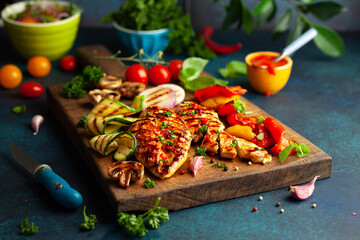 Grilled chicken breasts and different vegetables ad mushroom cooked on a BBQ served on wooden board. Close up view. Concept homemade summer barbeque dinner