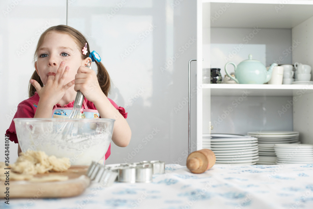 Wall mural Girl preparing food in bowl, using wire whisk and licking finger