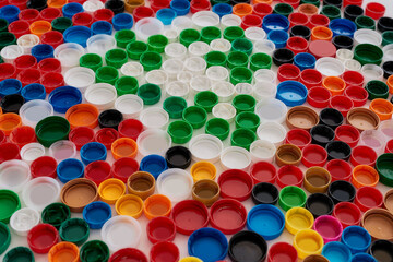 Close up of collage with colorful plastic bottle caps and recycling sign on white background. Reuse of waste concept.