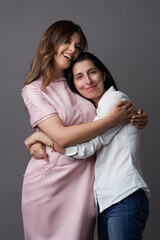 Two women are hugging on grey background with copy space