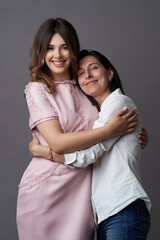 Fototapeta premium Two women are hugging on grey background with copy space