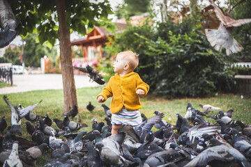 Cute little kid playing and feeding pigeons in the park
