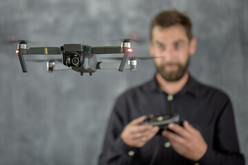 Happy man testing quadcopter. Remote unmanned aerial vehicle with camera. Male holding radio controller. Modern entertainment. Selective focus. A young adult man plays with a quadrocopter and has fun.