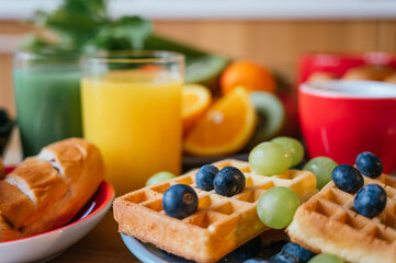 Healthy breakfast of waffles with blackberries, orange juice, coffee, croissant, fresh fruit and green juice on a wooden table