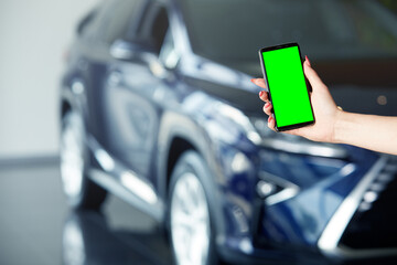 A woman's hand holds a mobile phone with a green screen. The girl uses a mobile phone. Chromakey, close-up of a woman hand holding a phone with a vertical green screen on the background of a car