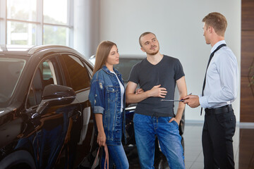 Selective focus a car dealership Manager shows a luxury car to a couple in a car dealership. The concept of professionalism, the lease agreement, car rental, retail sales