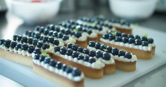 Women's hands decorate a cream dessert with blueberries on the kitchen table. Close up
