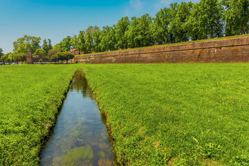 A view along a water channel towards the city walls of Lucca Italy in summer - obrazy, fototapety, plakaty