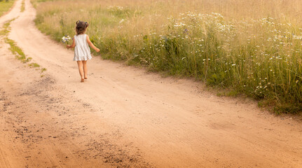 Little cute girl 1-3 in a light dress running on a path in the field on a background of grass with a bouquet of daisies