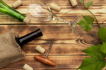 Wine glass, corkscrew, corks, wine bottles, grapevine on rustic burnt wooden background. Top view. Copy space