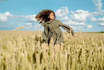 ears of wheat. young girl in dress shows emotion. emotionally jumps and runs on a summer field with spikelets. Hair flying in the wind, lifestyle Concept of cosmetology, harvest, farm