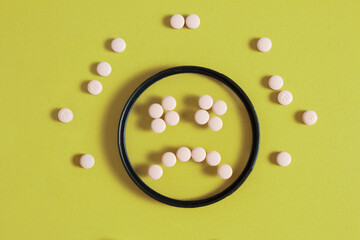 A sad smiley face made up of pills in a circular filter with medications around on a vivid yellow background.
