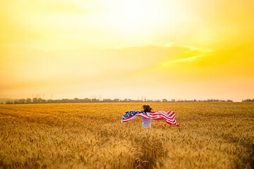 Woman running and jumping carefree with open arms over wheat field Holding USA flag.