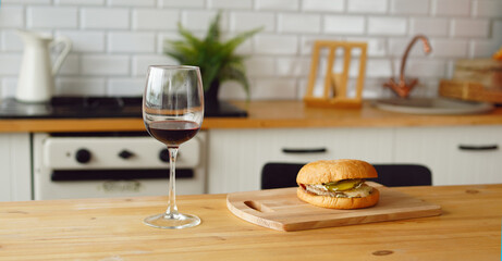 Close up of glass of wine with burger on wooden board on table in kitchen.