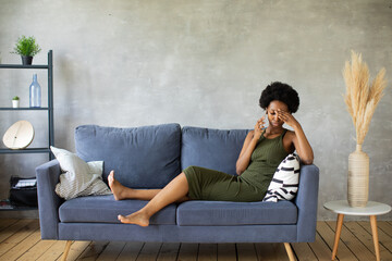 Unhappy African American woman talking on the phone, angry girl talking on the phone, discharged or broken mobile device, problem with phone, sitting on sofa